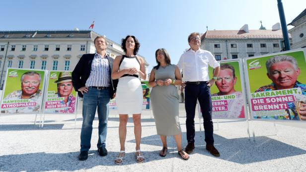 Vier Personen posieren vor Wahlplakaten der Grünen mit dem Slogan „Sakrament, die Sonne brennt!“.