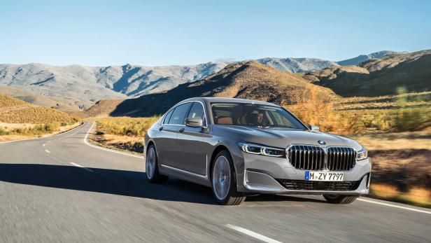 Ein grauer BMW der 7er-Reihe fährt auf einer Landstraße vor einer Bergkulisse.