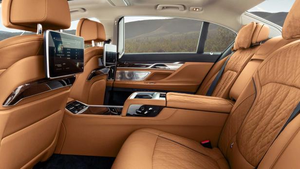 Der luxuriöse Innenraum eines Autos mit braunen Ledersitzen und Bildschirmen im Fond.