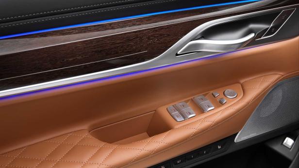 Die Türverkleidung eines Autos mit braunem Leder und Holzdetails sowie blauer Ambientebeleuchtung.