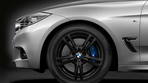 Detailansicht eines silbernen BMW mit schwarzen Felgen und blauen Bremssätteln.