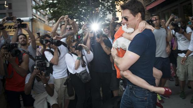 Tom Cruise trägt ein Kind auf dem Arm, umringt von Fotografen.