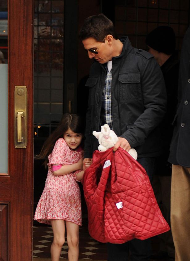 Tom Cruise hält die Hand seiner Tochter, die ein Kleid und einen Stoffhasen trägt.