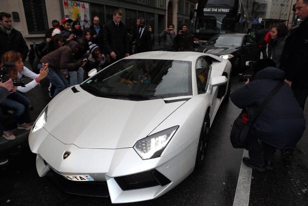 Ein weißer Lamborghini wird von Fotografen auf der Straße umringt.