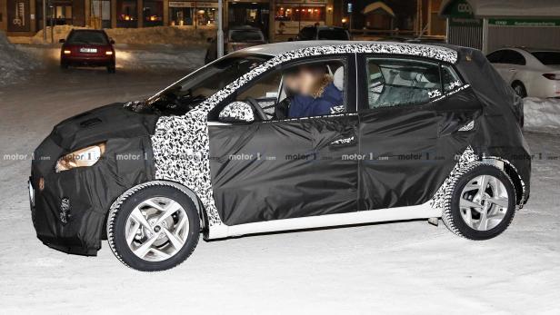 Ein getarntes Auto fährt auf einer verschneiten Straße.