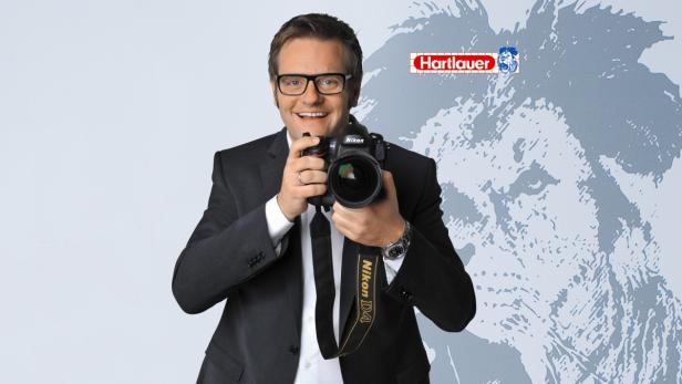 Ein lächelnder Mann mit Brille und Anzug hält eine Nikon D4 Kamera.