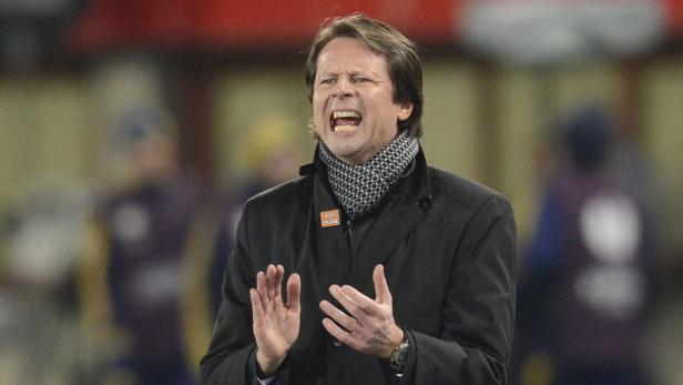 Ein Mann in einem schwarzen Mantel gestikuliert und schreit.