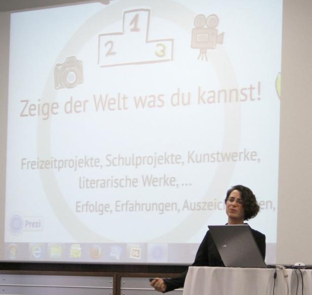 Eine Frau präsentiert vor einer Leinwand mit der Aufschrift „Zeige der Welt was du kannst!“.