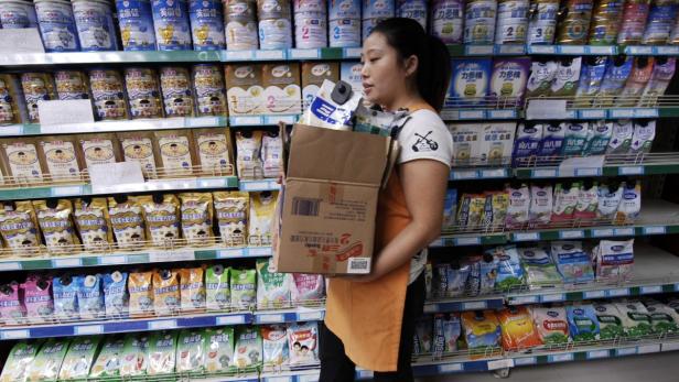 Eine Frau trägt einen Karton mit Babymilchpulver vor einem Regal im Supermarkt.