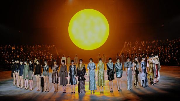 Models präsentieren Mode vor einem großen, gelben Kreis und Publikum.