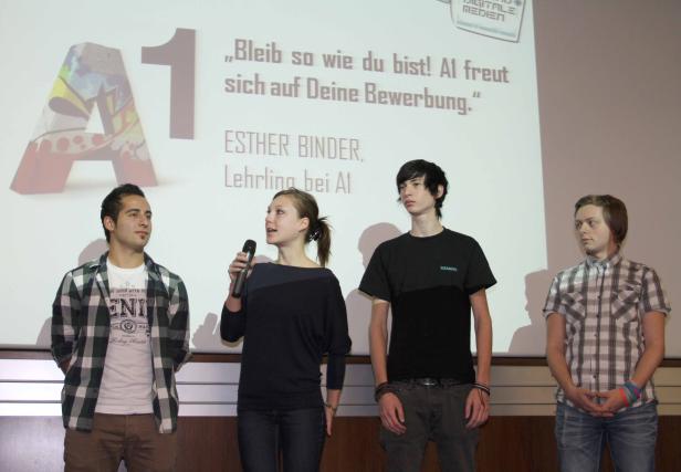 Vier junge Leute stehen vor einer Leinwand mit dem A1-Logo und dem Slogan „Bleib so wie du bist! A1 freut sich auf Deine Bewerbung.“.