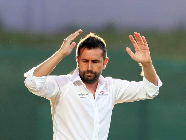 Ein Mann im weißen Hemd hebt die Hände vor einem Fußballspiel in Österreich.