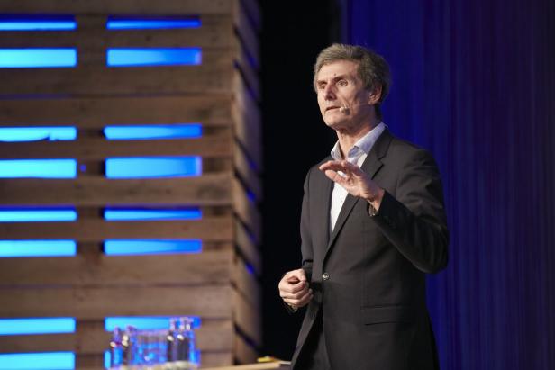 Ein Mann in einem Anzug hält eine Rede vor einem Publikum.