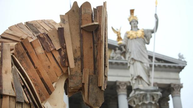 Ein Trojanisches Pferd aus Holz steht vor der Pallas-Athene-Statue in Wien.