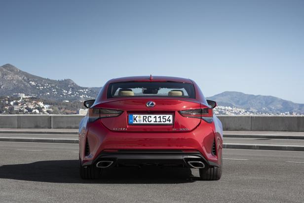 Die Rückansicht eines roten Lexus RC 300h vor einer Küstenlandschaft.