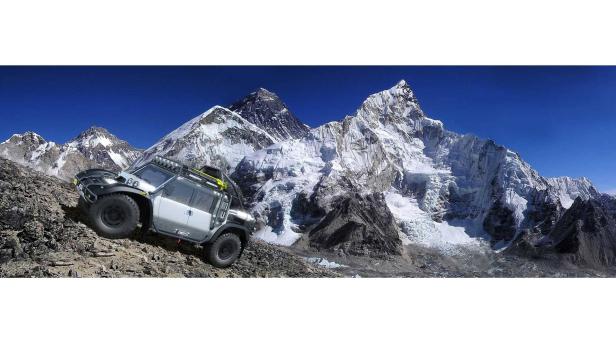 Ein Geländewagen fährt einen steinigen Hang hinauf, im Hintergrund schneebedeckte Berge.