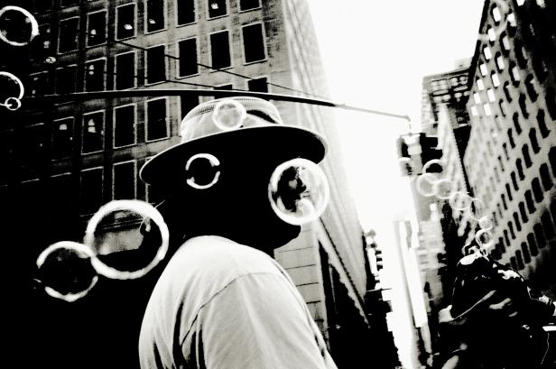 Ein Mann mit Hut pustet Seifenblasen in einer städtischen Umgebung.