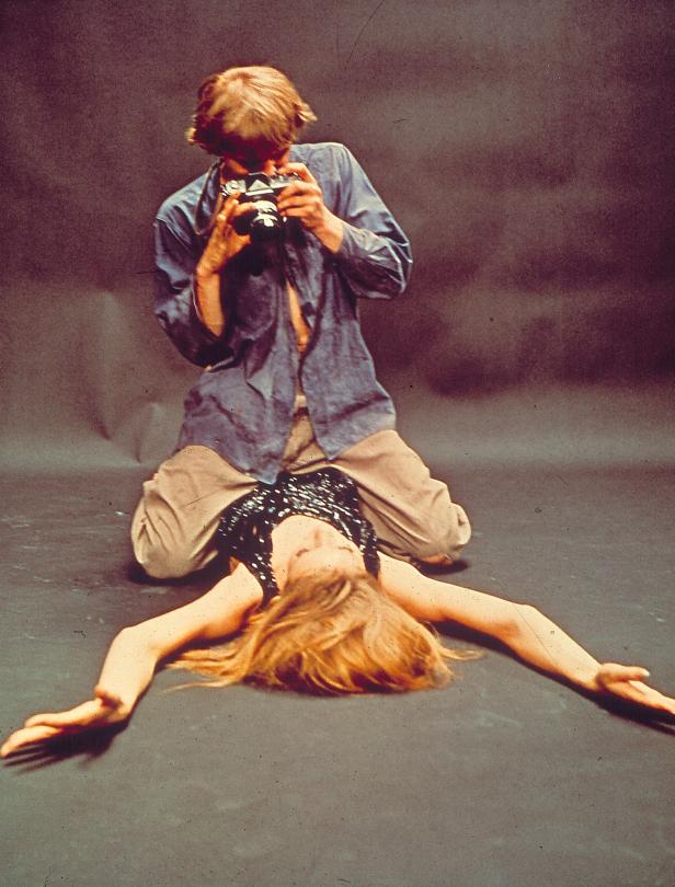 Ein Mann kniet und fotografiert eine am Boden liegende Frau.