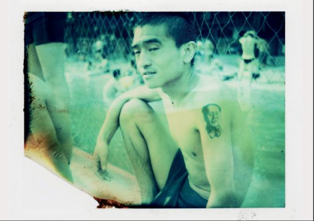 Ein junger Mann sitzt mit einem Mao-Tattoo auf dem Arm.