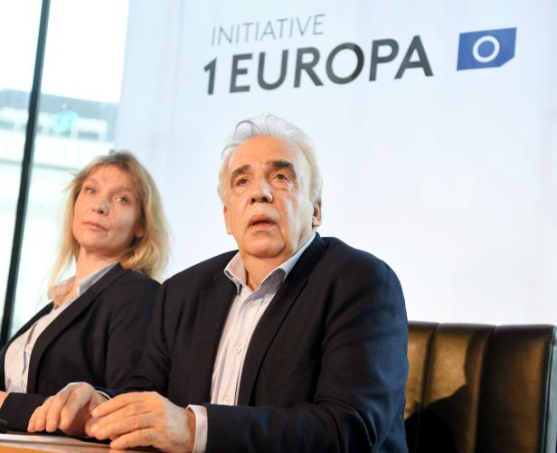 Ein Mann und eine Frau sitzen vor einem Banner der Initiative „1 Europa“.