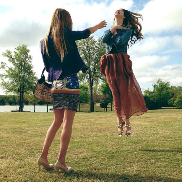 Eine Frau springt lachend in die Luft, während eine andere Frau sie mit ausgestrecktem Arm erwartet.