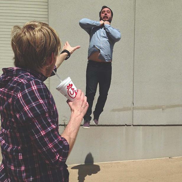 Ein Mann trinkt aus einem Chick-fil-A-Becher, während ein anderer Mann im Hintergrund zu schweben scheint.