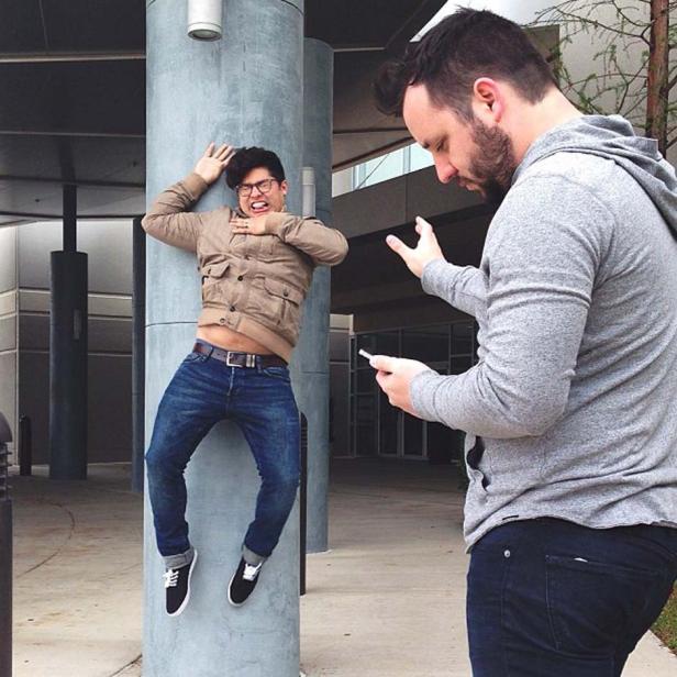 Ein Mann umarmt einen Pfeiler, während ein anderer Mann mit einem Handy in der Hand daneben steht.