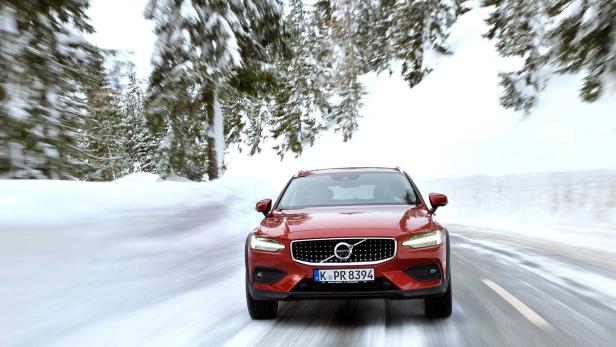 Ein roter Volvo fährt auf einer schneebedeckten Straße durch einen Winterwald.