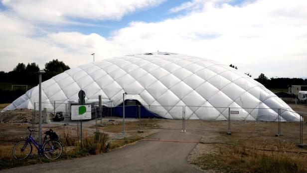 Eine große, weiße Traglufthalle auf einem Feld, umgeben von einem Zaun.