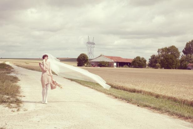 Eine Frau in einem Kleid und Schleier steht auf einem Feldweg.