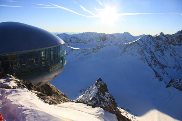 Ein futuristisches Gebäude auf einem Berg mit Blick auf schneebedeckte Gipfel.