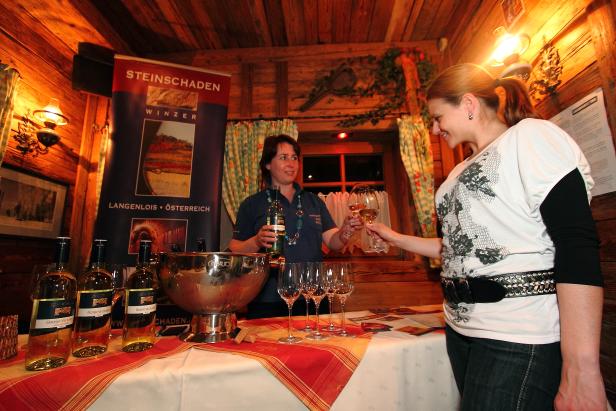 Eine Frau reicht einer anderen ein Glas Wein in einem rustikalen Ambiente.