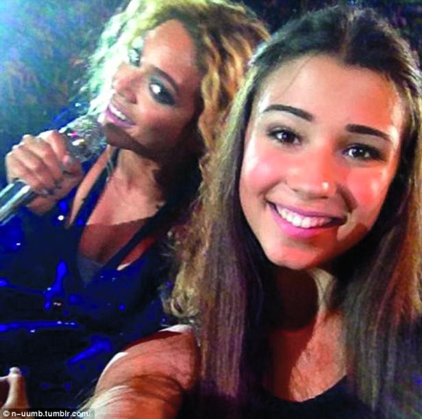 Eine junge Frau macht ein Selfie mit Beyoncé, die ein Mikrofon hält.