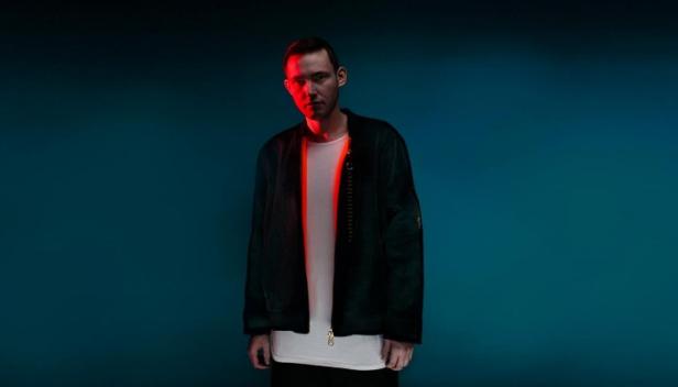 Ein Mann mit Jacke vor einem blaugrünen Hintergrund, beleuchtet mit rotem Licht.