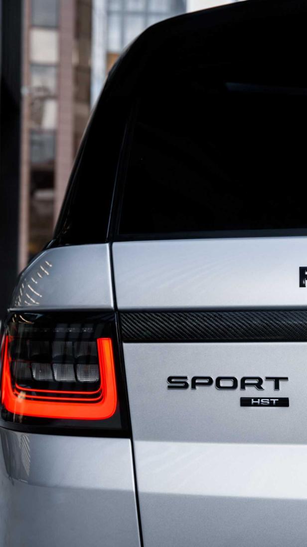 Die Rückansicht eines silbernen Range Rover Sport HST mit leuchtenden Rückleuchten.
