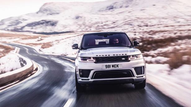 Ein silberner Range Rover fährt auf einer kurvenreichen Straße in einer verschneiten Landschaft.