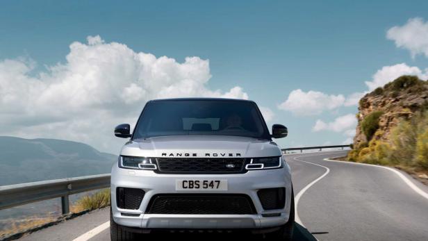 Ein silberner Range Rover fährt auf einer kurvenreichen Straße in einer bergigen Landschaft.