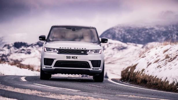 Ein silberner Range Rover fährt auf einer kurvigen Straße in einer verschneiten Landschaft.