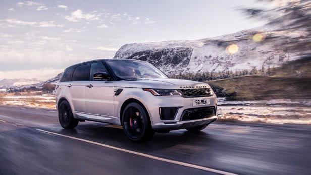 Ein silberner Range Rover fährt auf einer Straße vor einer verschneiten Berglandschaft.