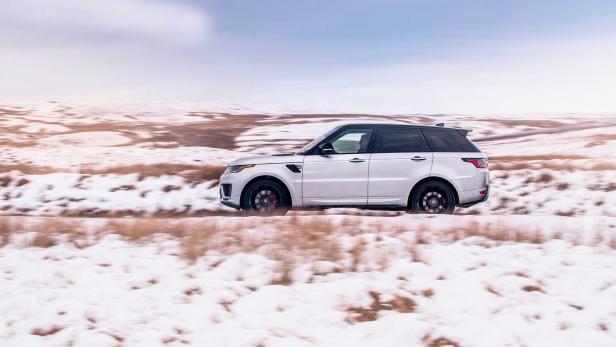 Ein silberner Range Rover Sport fährt auf einer schneebedeckten Straße.