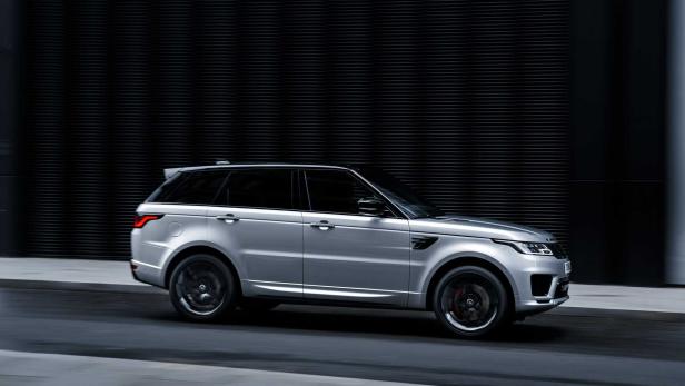 Ein silberner Range Rover Sport fährt auf einer dunklen Straße.