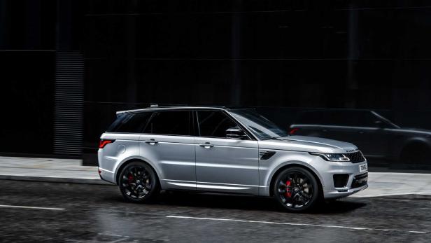 Ein silberner Range Rover Sport fährt auf einer dunklen Straße.