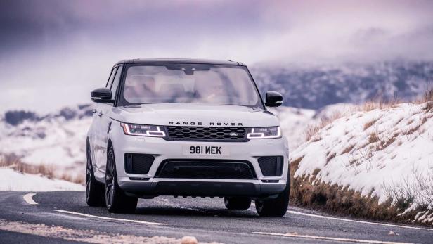 Ein silberner Range Rover fährt auf einer verschneiten Straße.