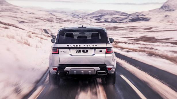Ein silberner Range Rover Sport fährt auf einer Straße durch eine verschneite Landschaft.