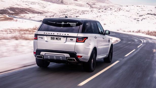 Ein silberner Range Rover Sport fährt auf einer kurvigen Straße durch eine verschneite Landschaft.
