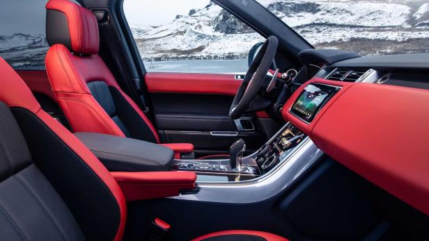 Innenansicht eines Range Rover mit roten Ledersitzen und schneebedeckten Bergen im Hintergrund.