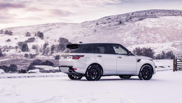 Ein silberner Range Rover Sport steht im Schnee vor einer verschneiten Hügellandschaft.