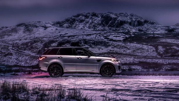 Ein silberner Range Rover steht in einer verschneiten Landschaft vor einem Berg.