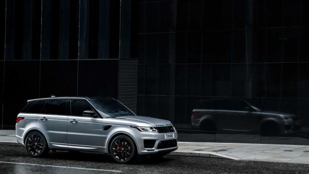 Ein silberner Range Rover Sport steht vor einem modernen Gebäude mit dunkler Glasfassade.