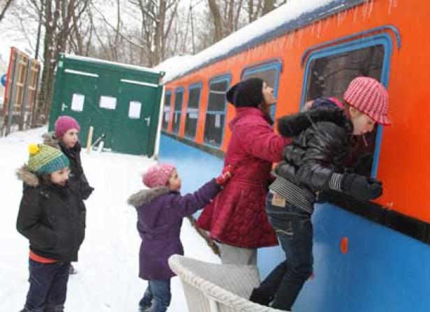 Eine Gruppe Kinder spielt im Schnee an einem orangefarbenen Zugwagen.